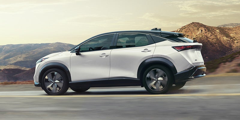Nissan Ariya driving through the desert on the road as the sun is setting in front of the vehicle
